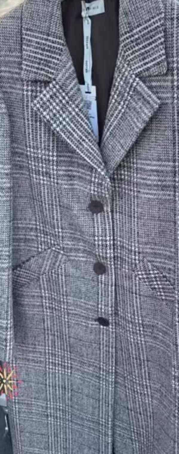 Cappotto lungo a quadri con spilla, appeso in negozio