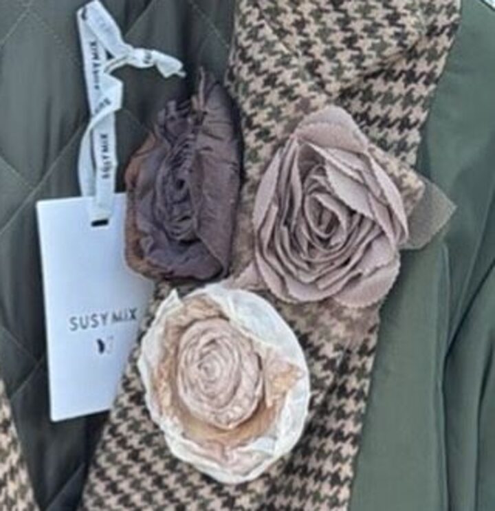 Dettaglio di un cappotto pied-de-poule con spille a fiore in tessuto